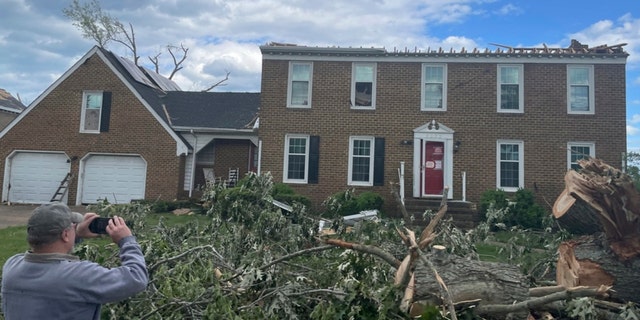 A man photographs a home damaged by a tornado in Virginia Beach