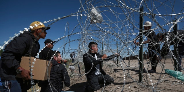 Migrants cross the barbed-wire barrier into the United States