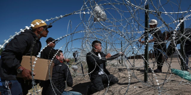 Migrants cross a barbed-wire barrier into the United States