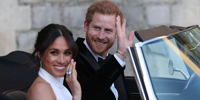 Meghan Markle in a white dress and Prince Harry in a suit waving from their car