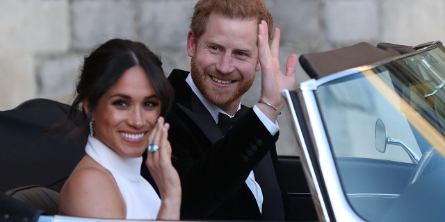 Meghan Markle in a white dress and Prince Harry in a suit waving from their car