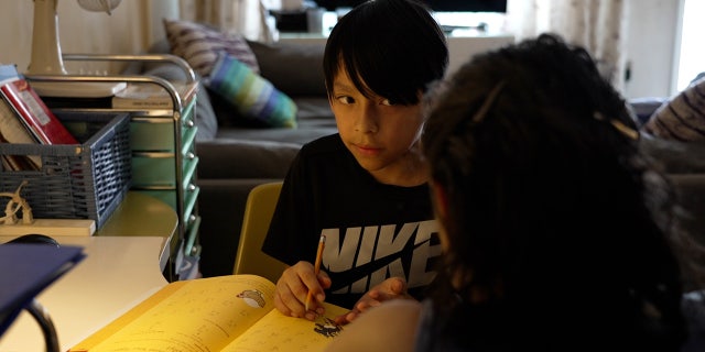 Homeschool mother and her son sit with math workbook open between them