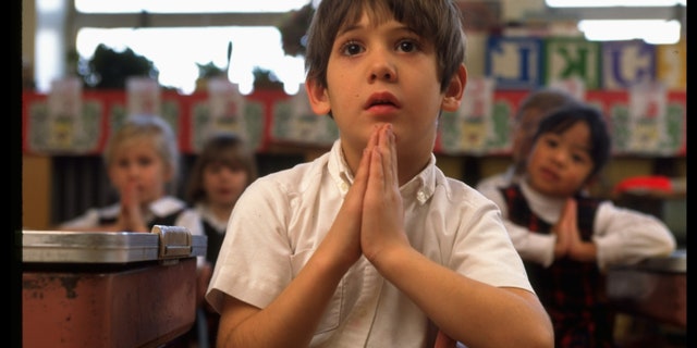 Faith dilemma in focus: 'It's Sunday and I haven't gone to church — what do I do?' Boy clasping hands, saying prayers in first grade class at St. Gertrude's elementary school.