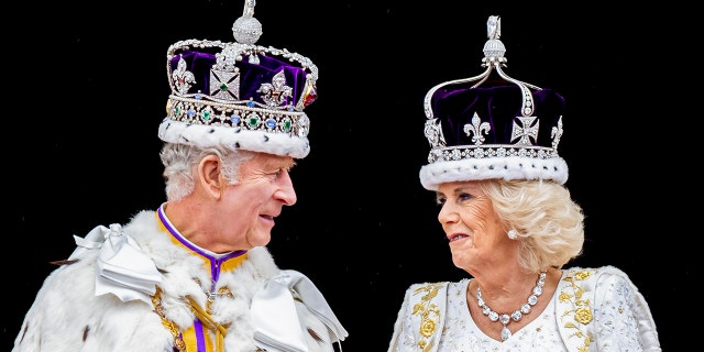 King Charles in his royal regalia looking at Camilla in a white gown wearing a crown