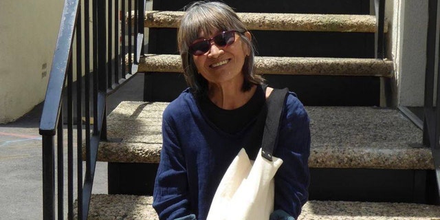 MASH star Eileen Saki wears blue sweater and carries canvas tote while perched on staircase