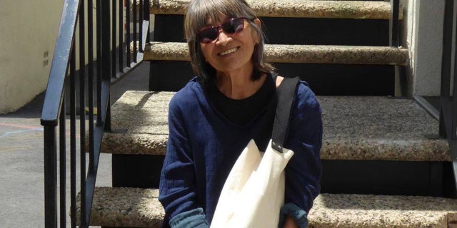 MASH star Eileen Saki wears blue sweater and carries canvas tote while perched on staircase