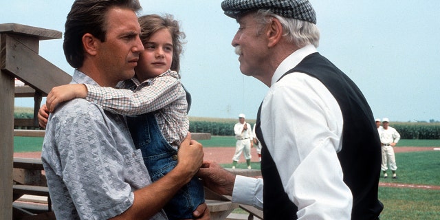 Kevin Costner and Gabby Hoffman stand in front of baseball diamond in a Field of Dreams scene