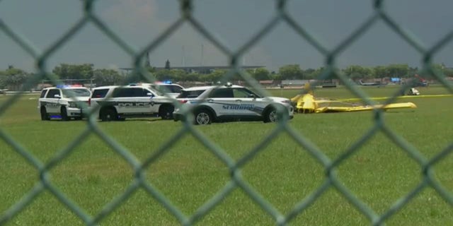 Veículos de segurança do aeroporto são vistos ao lado do avião acidentado através de uma cerca de arame