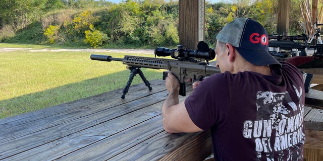 A man wearing Gun Owners of America merchandise shoots a rifle