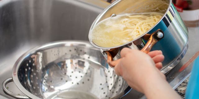 Woman separates water from spaghetti with an empty metal colander.