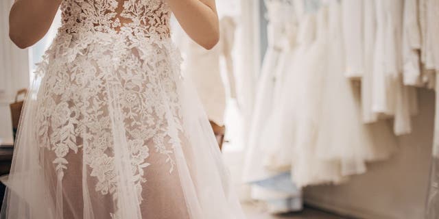 Woman tries on see-through lace weeding gown in a store.