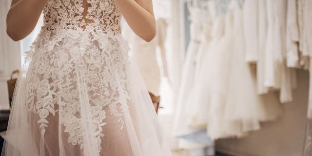 Woman tries on see-through lace weeding gown in a store.