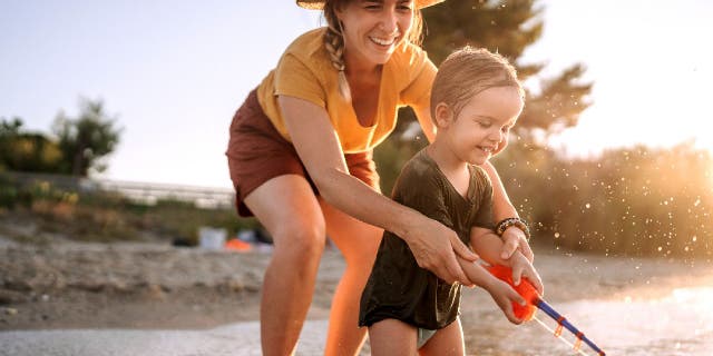 Mother and cute little toddler playing with fishing toy on the sea.