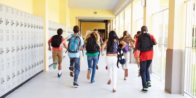 Group of high school students running down corridor.