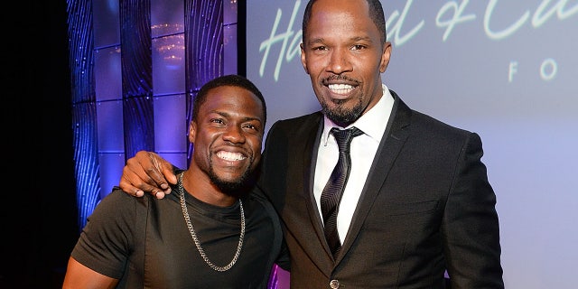 Jamie Foxx wears a black tuxedo with Kevin Hart wearing a black shirt at celebrity event.