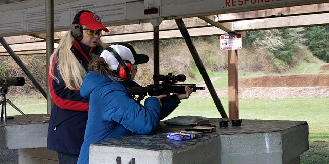Firearms instructor helps woman aim AR-15 at outdoor rifle range