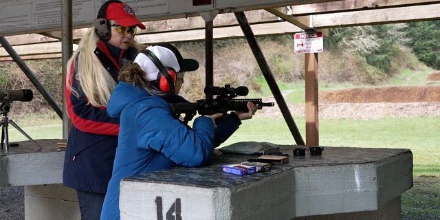 Firearms instructor helps woman aim AR-15 at outdoor rifle range