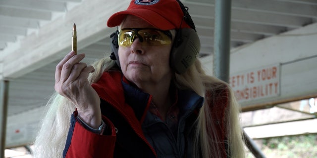 A female firearms instructor holds up a bullet for a bolt-action rifle