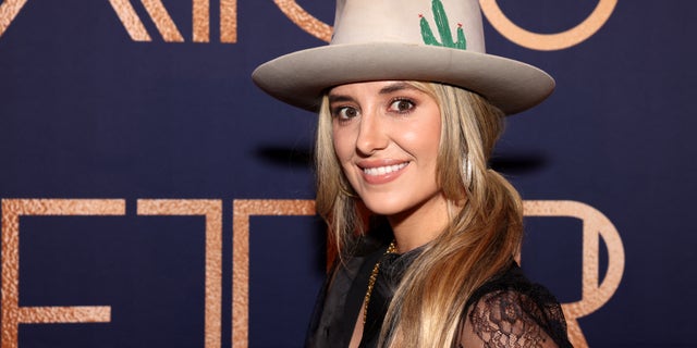 Lainey Wilson smiles for a photo wearing a large cowboy hat.