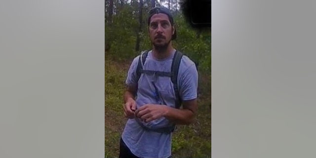 Michael Burham wearing a hat and backpack in the woods