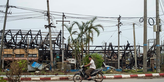 man rides motorbike past damaged buildings