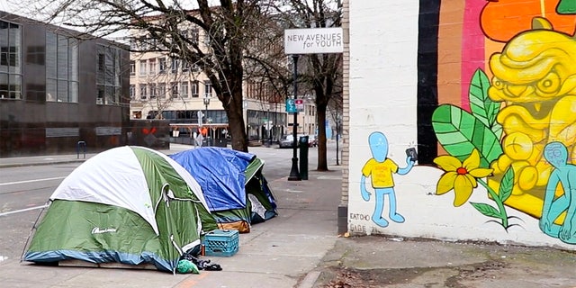 Tents cover a sidewalk in Portland next to a brightly-colored mural