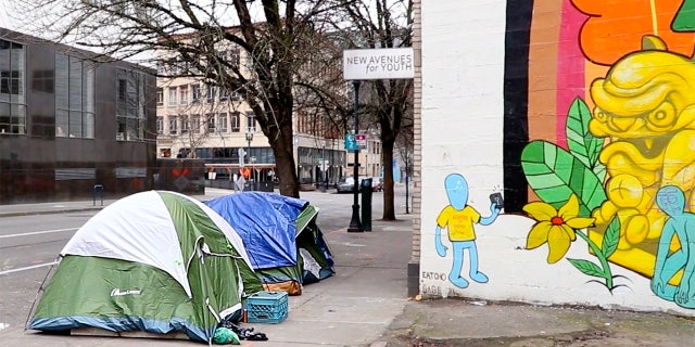 Tents cover a sidewalk in Portland next to a brightly-colored mural