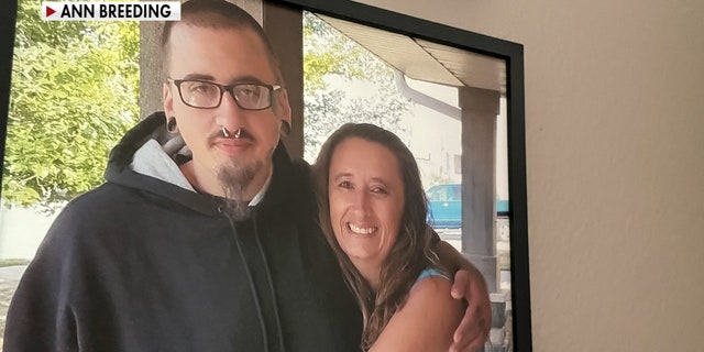 A young man in glasses wraps his arm around an older woman who is smiling and is his mother