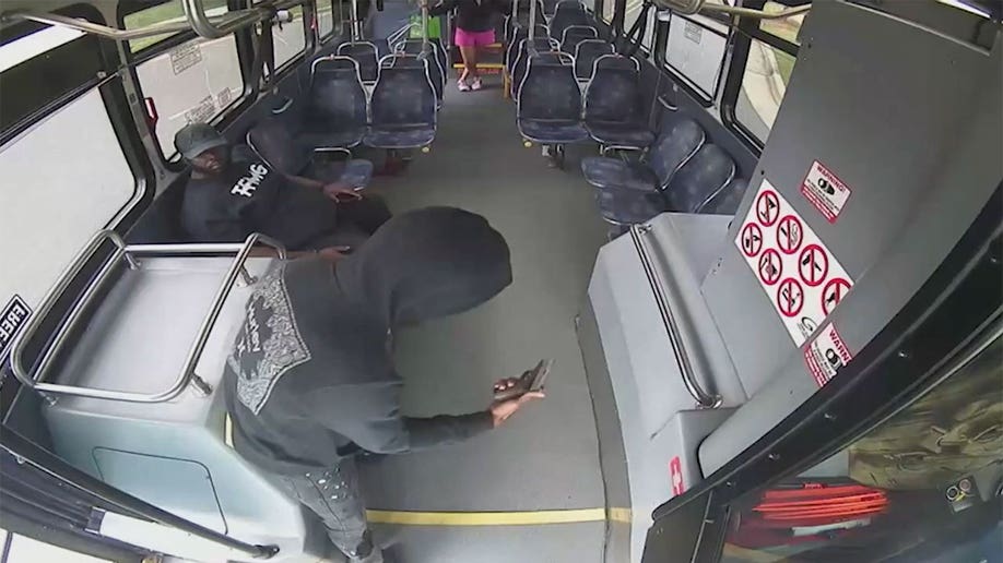 Man pulling out a gun at the front of a bus.