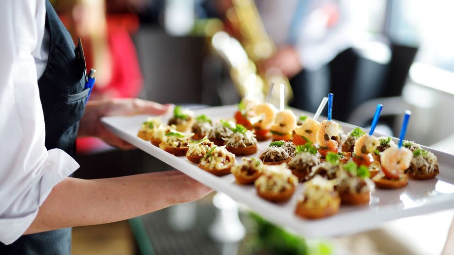 Waiter carries plates with meat appetizer on a tray at a wedding or special event.