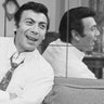 Ed Ames sitting next to a mirror and smiling