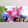 Two women wear large flower-like hats at the Kentucky Derby. One woman wears a pink hat while another woman wears a purple hat.