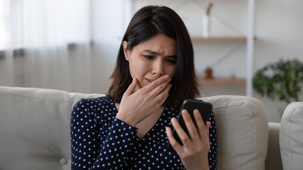 Woman visibly upset, looking at her phone.