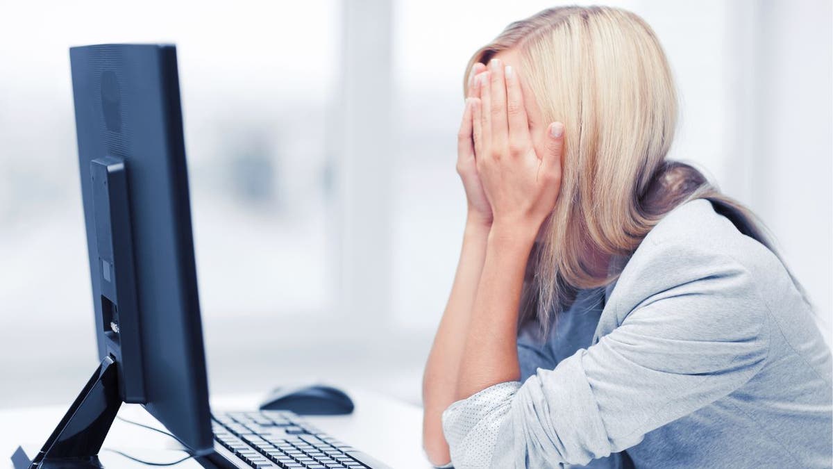 Woman with her hands over her face, sitting in front of her desktop computer.