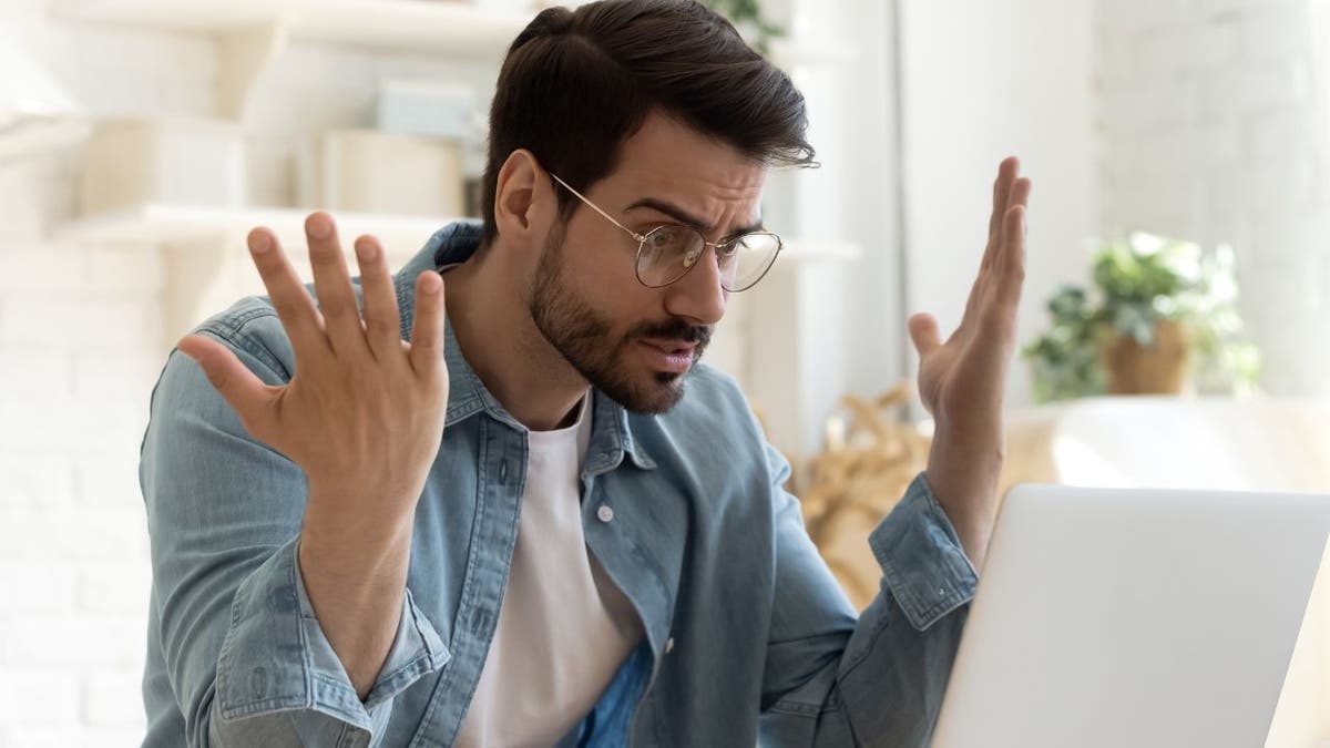 Man looking at his computer with his hands in the air.