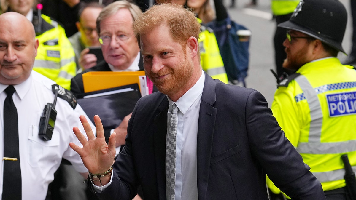 Prince Harry in a dark suit waving to a crowd