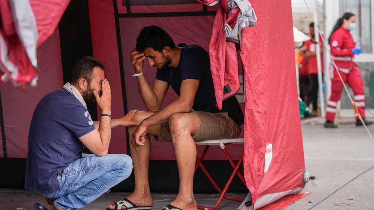 Survivors of a shipwreck react outside a warehouse at the port