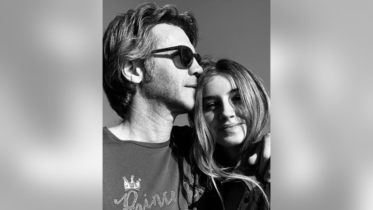 A close-up black and white photo of Prince Emanuele Filiberto wearing sunglasses and a dark shirt kissing his daughters forehead
