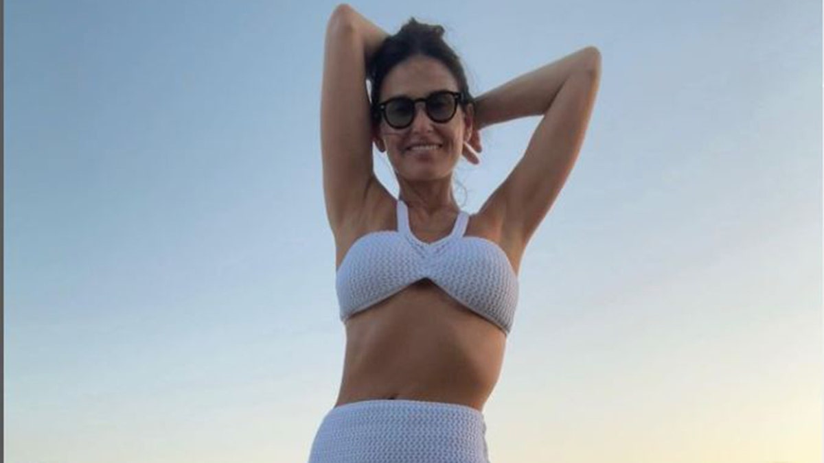 Demi Moore posing in a white bathing suit as the sun sets behind her