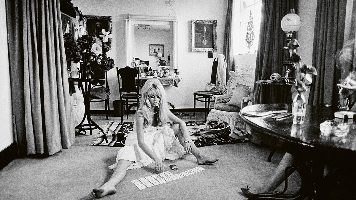 Brigitte Bardot wearing a white dress and playing cards on the floor