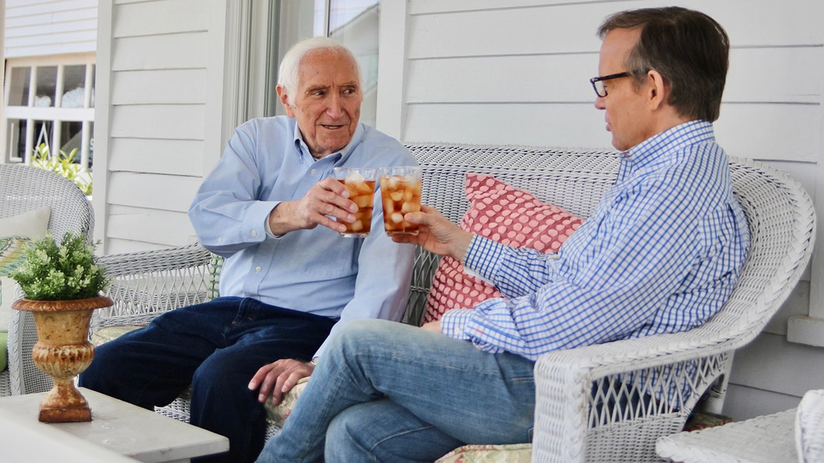 Gabe Briguglio and Eric Shawn wearing blue shirts cheers drinks on white couch outside