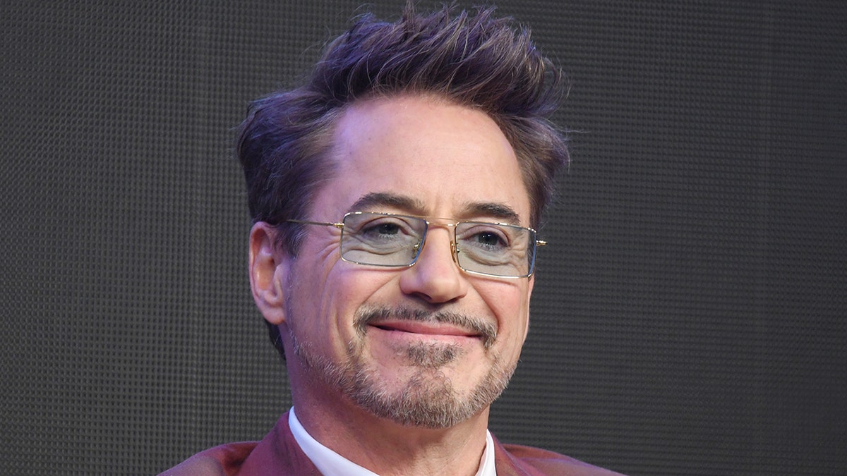 Robert Downey Jr. smiles with blue tinted retangular glasses on stage in Seoul, South Korea