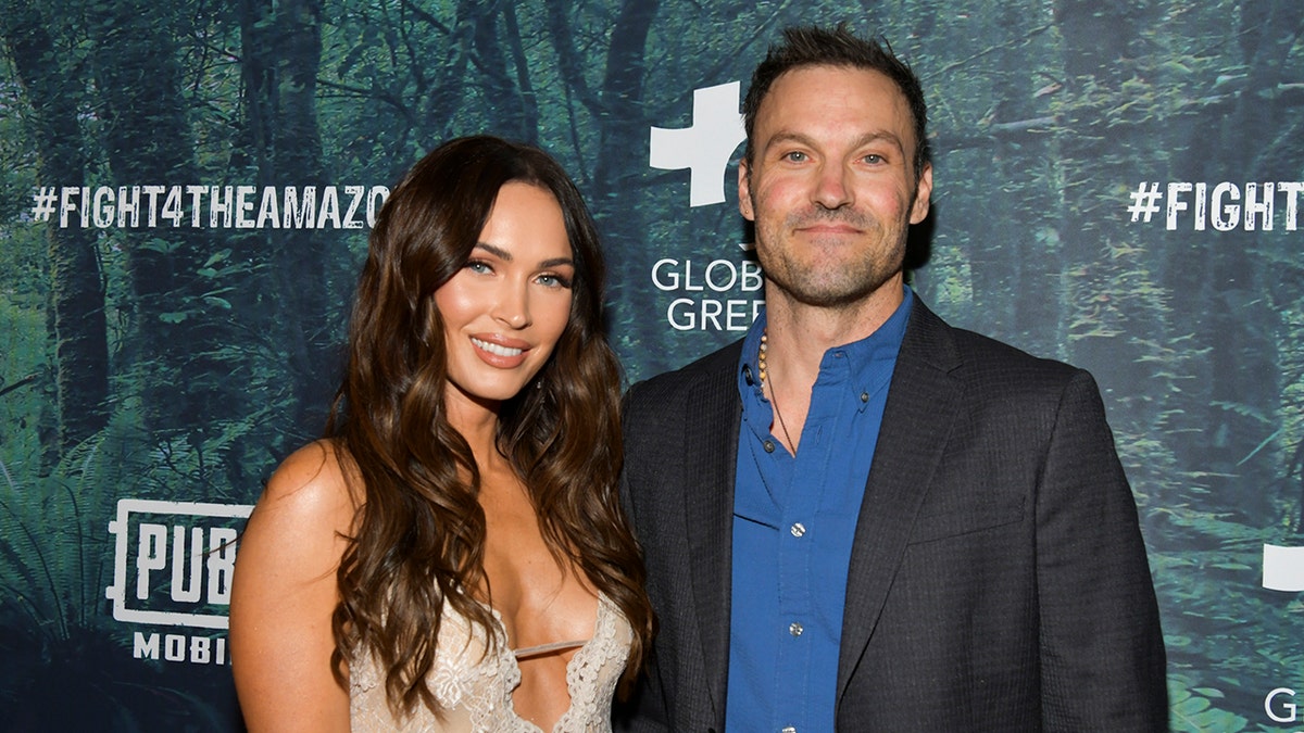 Megan Fox smiles on the red carpet with Brian Austin Green in a black jacket and blue shirt
