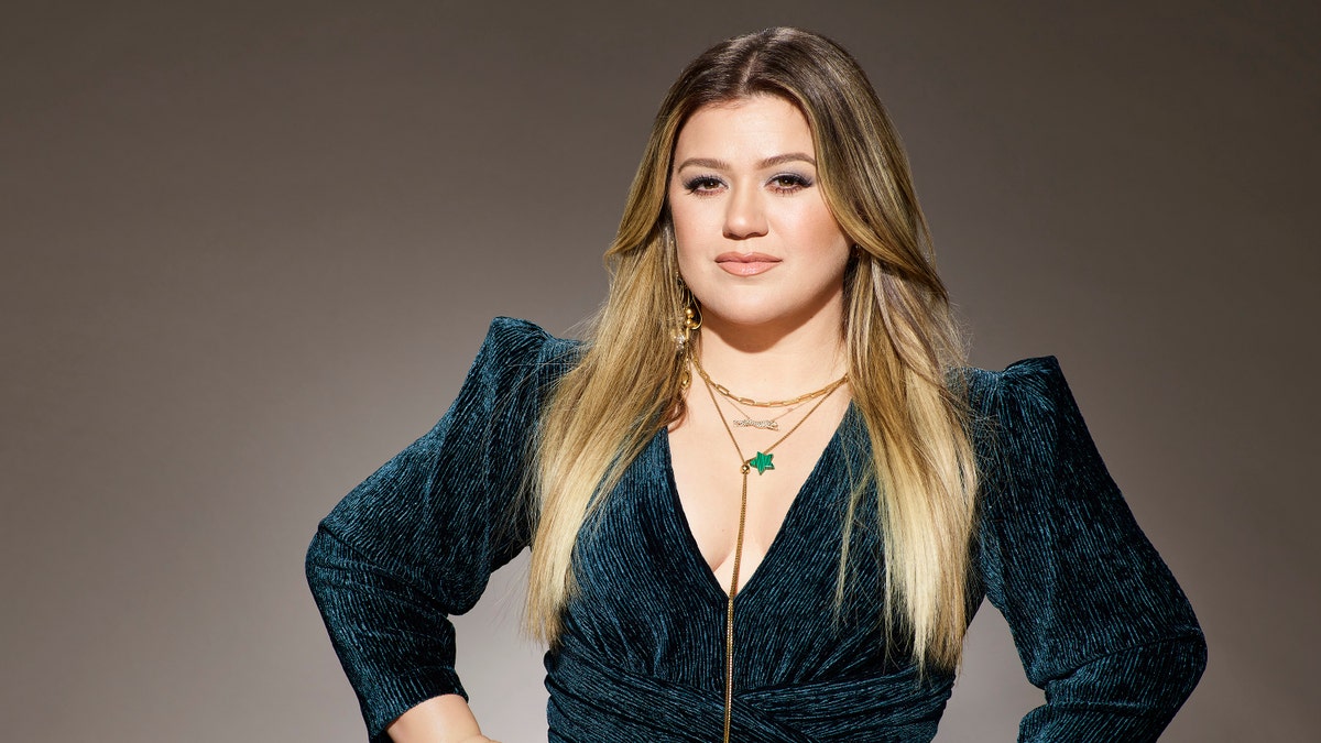 Kelly Clarkson in a green velvet dress with her hands on her hips for "The Voice" promotional pictures
