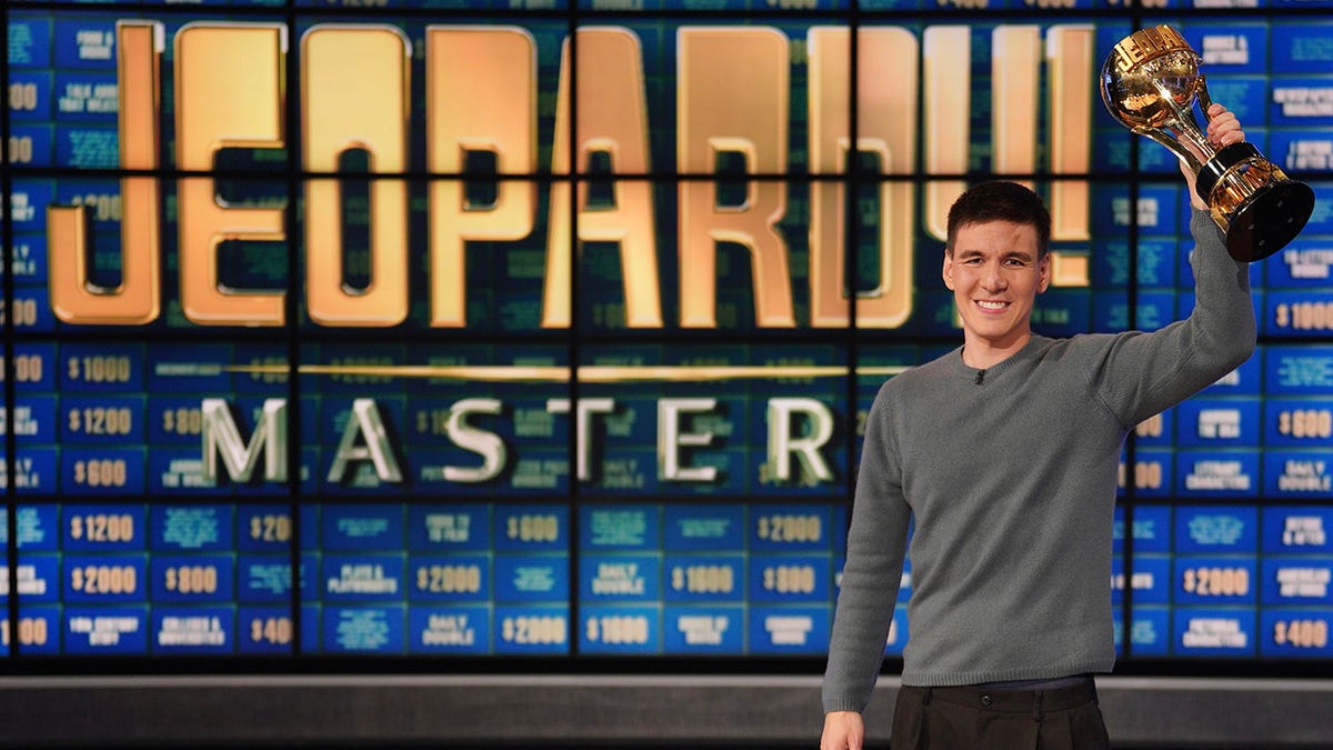 A photo of James Holzhauer holding a trophy on the "Jeopardy!" set