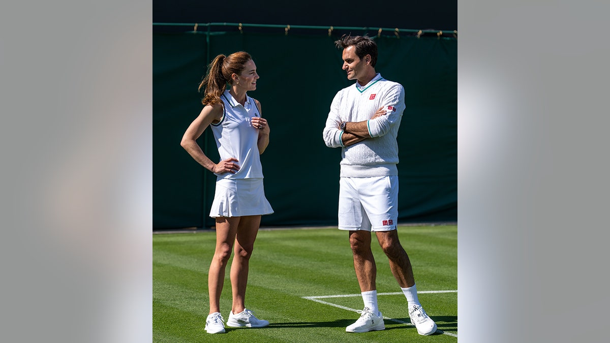 Kate Middleton with her hands on her hips in white talks with Roger Federer on the court of Wimbledon