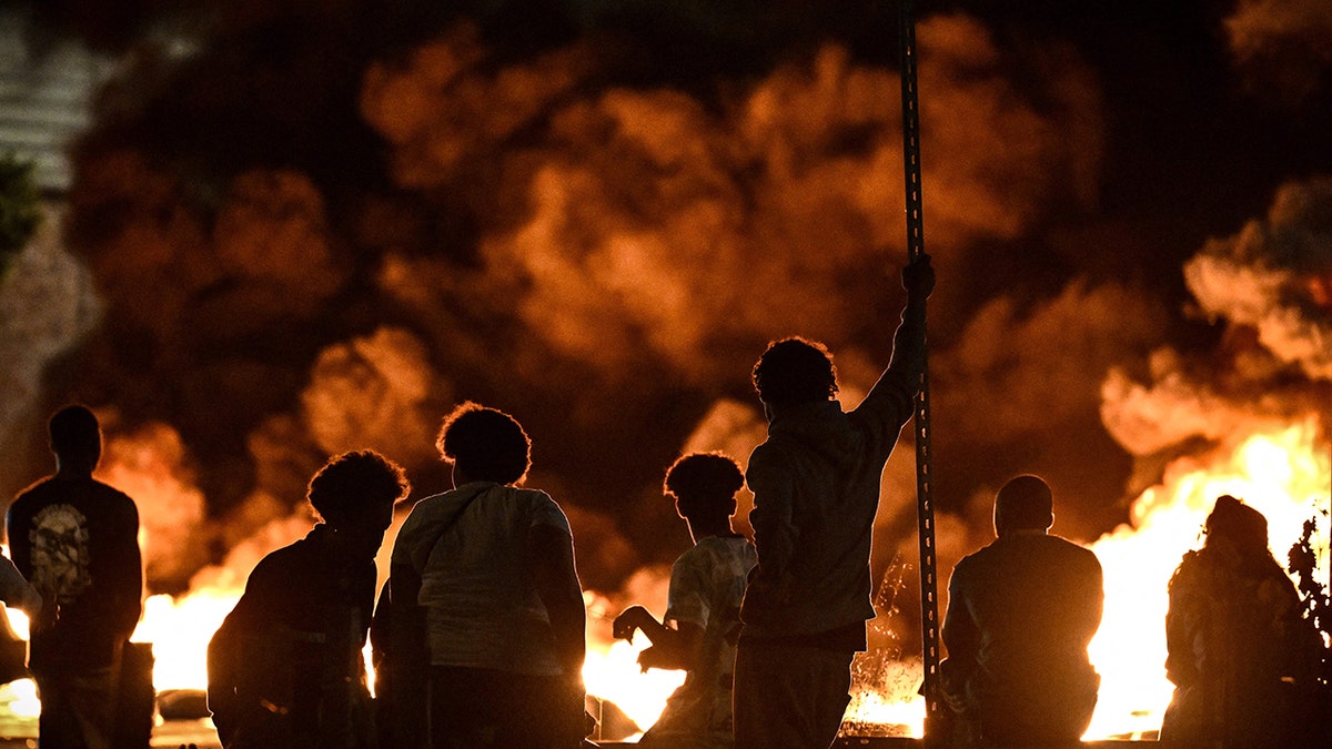Protesters stand in front of flames