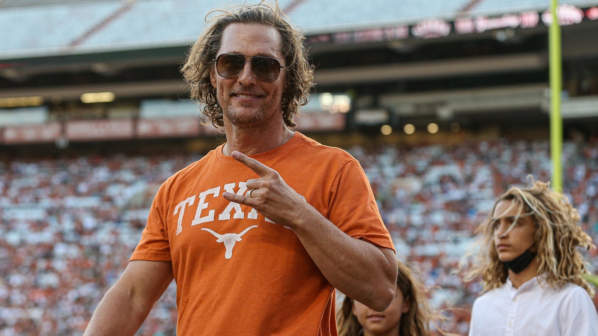 Matthew McConaughey wearing a Texas longhorns t-shirt and flashing the longhorns hand gesture