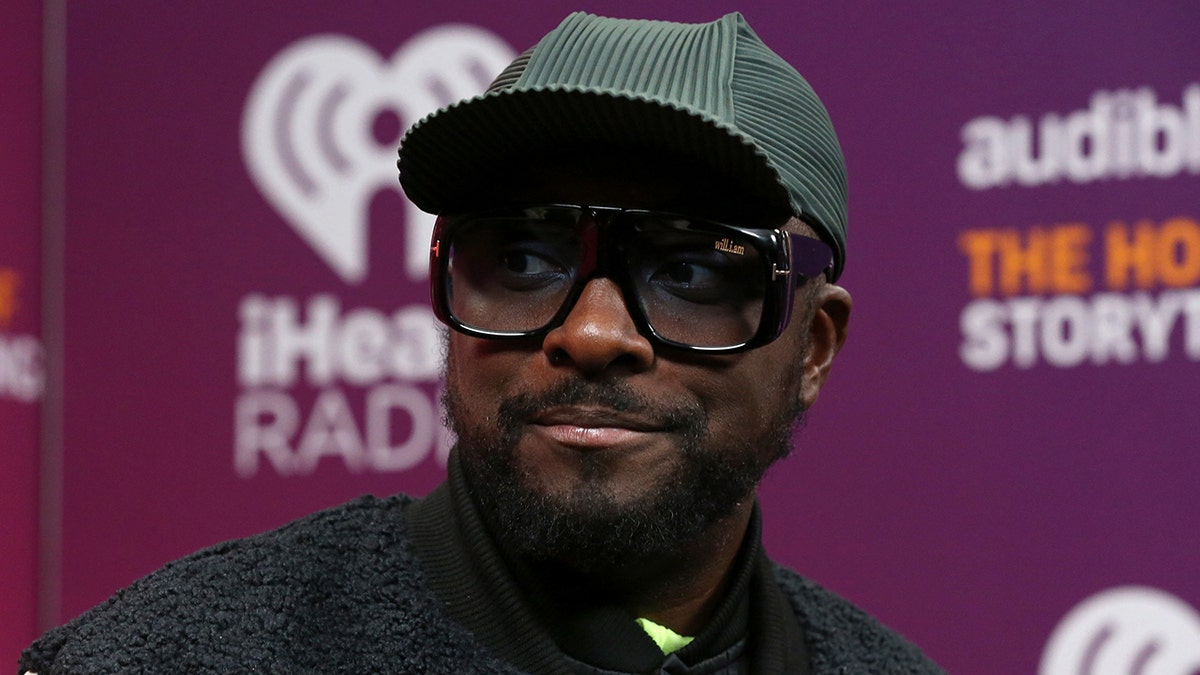 Will.I.am. wears a green hat at an IHeartRadio event and large glasses