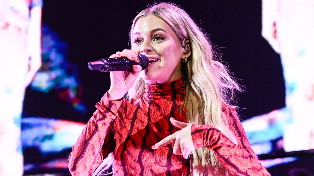 Kelsea Ballerini in a red patterned top singing into the microphone
